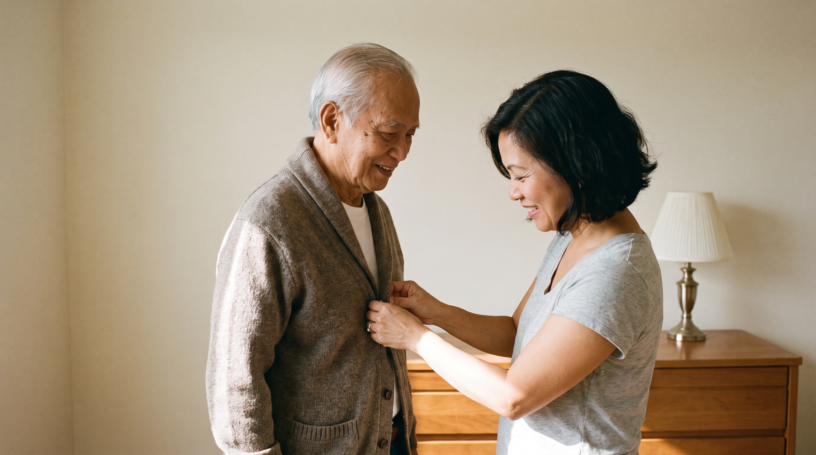 A daughter helps her father, in his 80s, button his cardigan